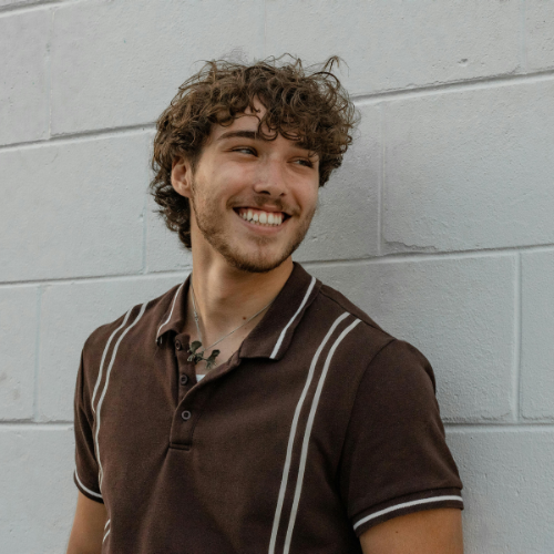 A man smiling and looking to the side while leaning against a white wall at MLB recovery